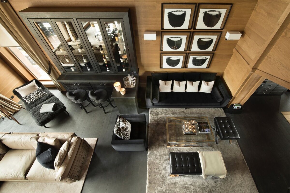 A chic, contemporary living room from above, featuring dark and light sofas, a sophisticated bar, modern art, and sleek furnishings.