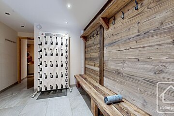 A ski boot room with a large boot dryer, a rustic wooden bench with coat hooks, and wooden paneling. Tiled floor.