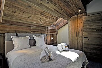 Cozy attic bedroom with rustic wooden walls and ceiling, a bed with white linens, and thoughtful touches like slippers and robes.