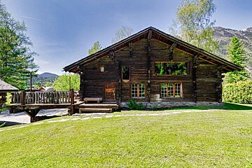 A large wooden house with a deck and mountains in the background
