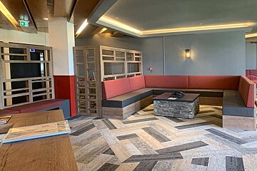 Modern lounge with a U-shaped red/gray bench, stone coffee table, and decorative wooden dividers. Features a patterned floor and warm recessed lighting.