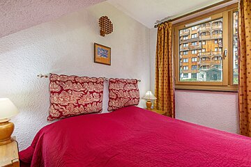 A bedroom with a red bed and a window