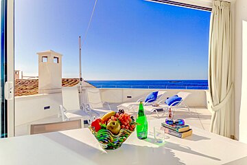 A bowl of fruit sits on a table in front of a window overlooking the ocean