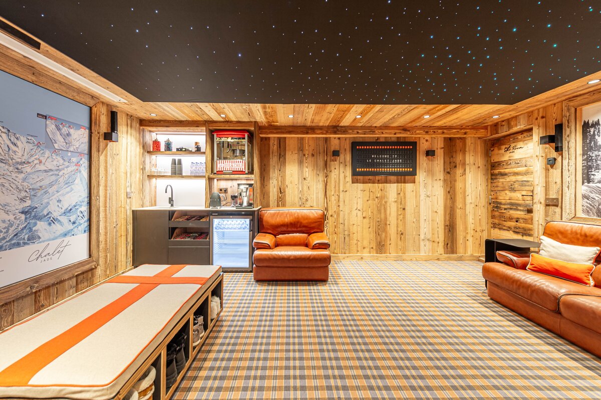 Cozy alpine chalet lounge featuring wood-paneled walls, leather seating, plaid carpet, a minibar, and a starry sky ceiling.