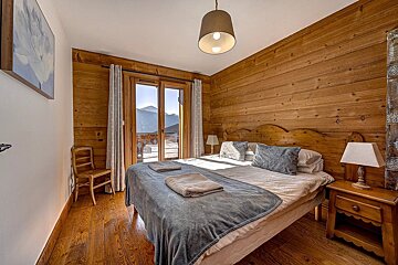 Cozy wooden bedroom with a large bed, rustic decor, and glass doors opening to a scenic mountain view.
