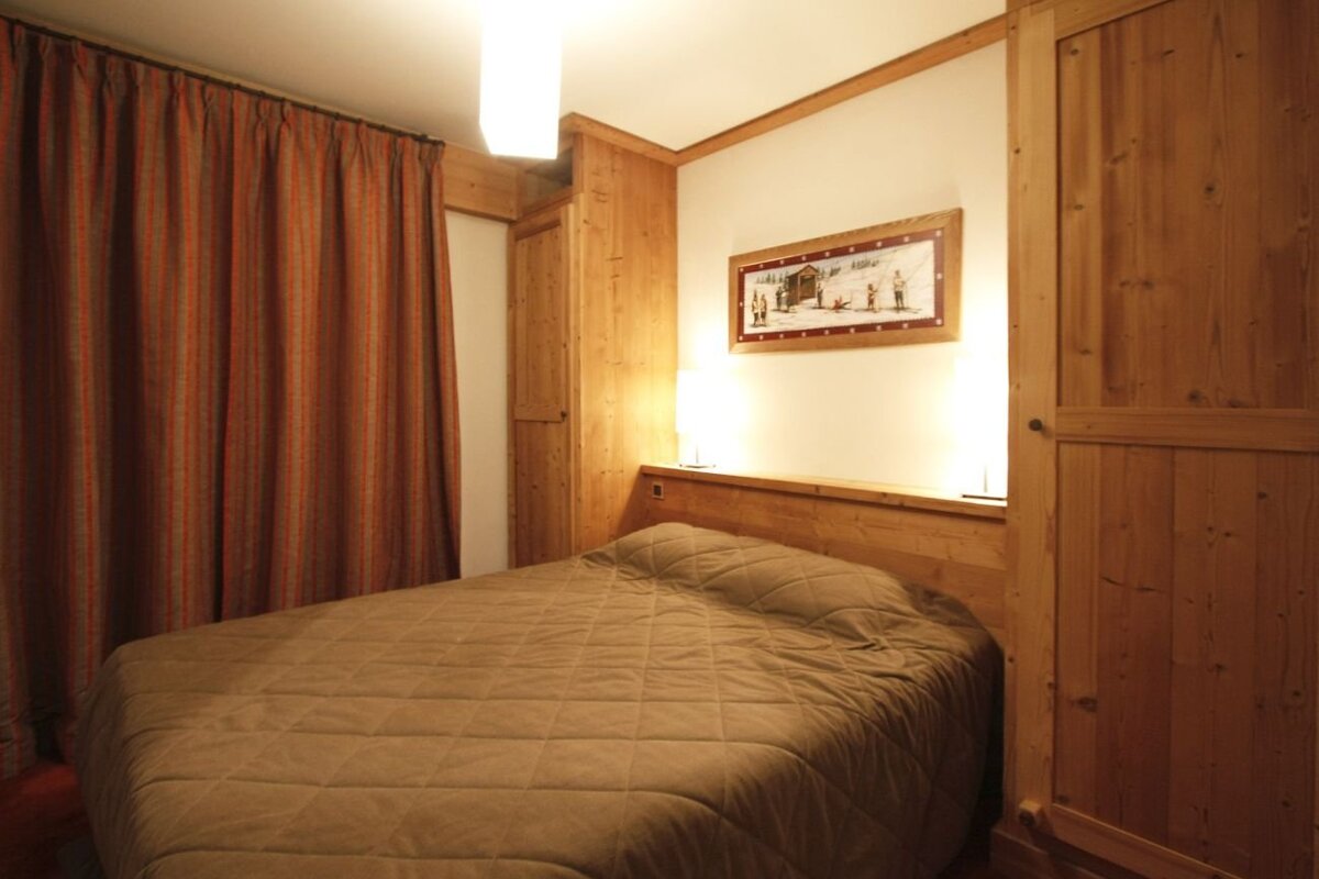 Cozy cabin-style bedroom with wood paneling, built-in wardrobes, a quilted brown bedspread, warm lighting, and striped curtains.