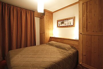 Cozy cabin-style bedroom with wood paneling, built-in wardrobes, a quilted brown bedspread, warm lighting, and striped curtains.