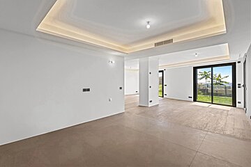 Spacious, modern empty room featuring white walls, warm cove lighting, and large sliding glass doors looking out to a garden.