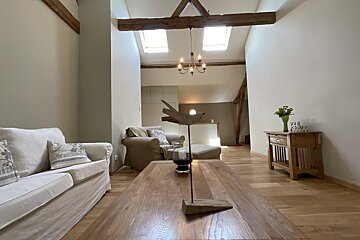 A cozy, bright living room features vaulted ceilings, exposed wooden beams, skylights, and a rustic wooden coffee table with a bird ornament.