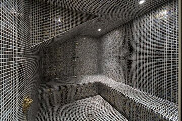 A modern dark gray mosaic-tiled steam room with built-in benches, a shower, and recessed lighting.