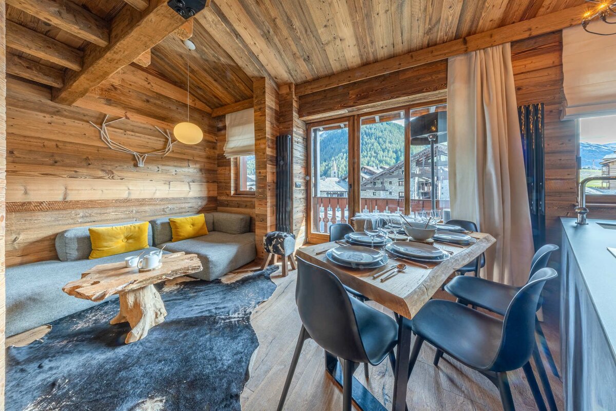 Rustic wooden chalet interior with a cozy lounge area, a set dining table, and scenic mountain views.