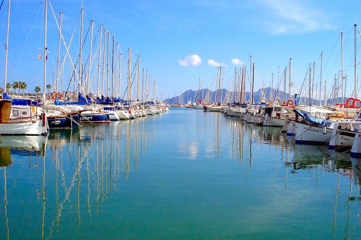 A row of boats are docked in a harbor and one of them has the name sandy on the side