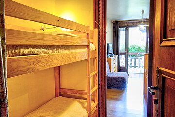 Wooden bunk beds in a cozy alcove, looking out to a bright living room with a balcony.
