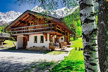 A house with mountains in the background and a tree in front of it