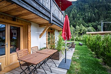 A wooden deck with a table and chairs and a red umbrella