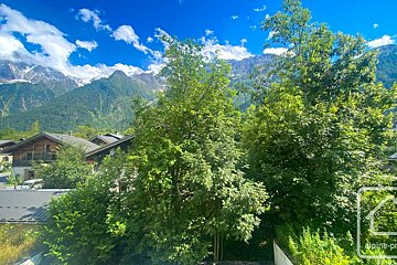 Snow-capped mountains under a clear blue sky, with traditional wooden houses and lush green trees in a picturesque valley.