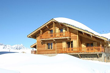A wooden house with a balcony is covered in snow