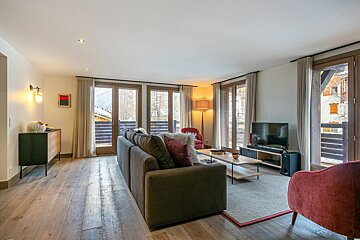 Cozy living room with a large sofa, TV, wooden floor, and multiple glass doors leading to balconies.