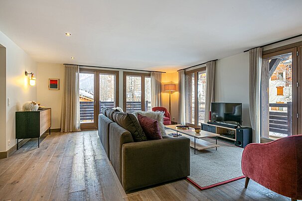 Cozy living room with a large sofa, TV, wooden floor, and multiple glass doors leading to balconies.