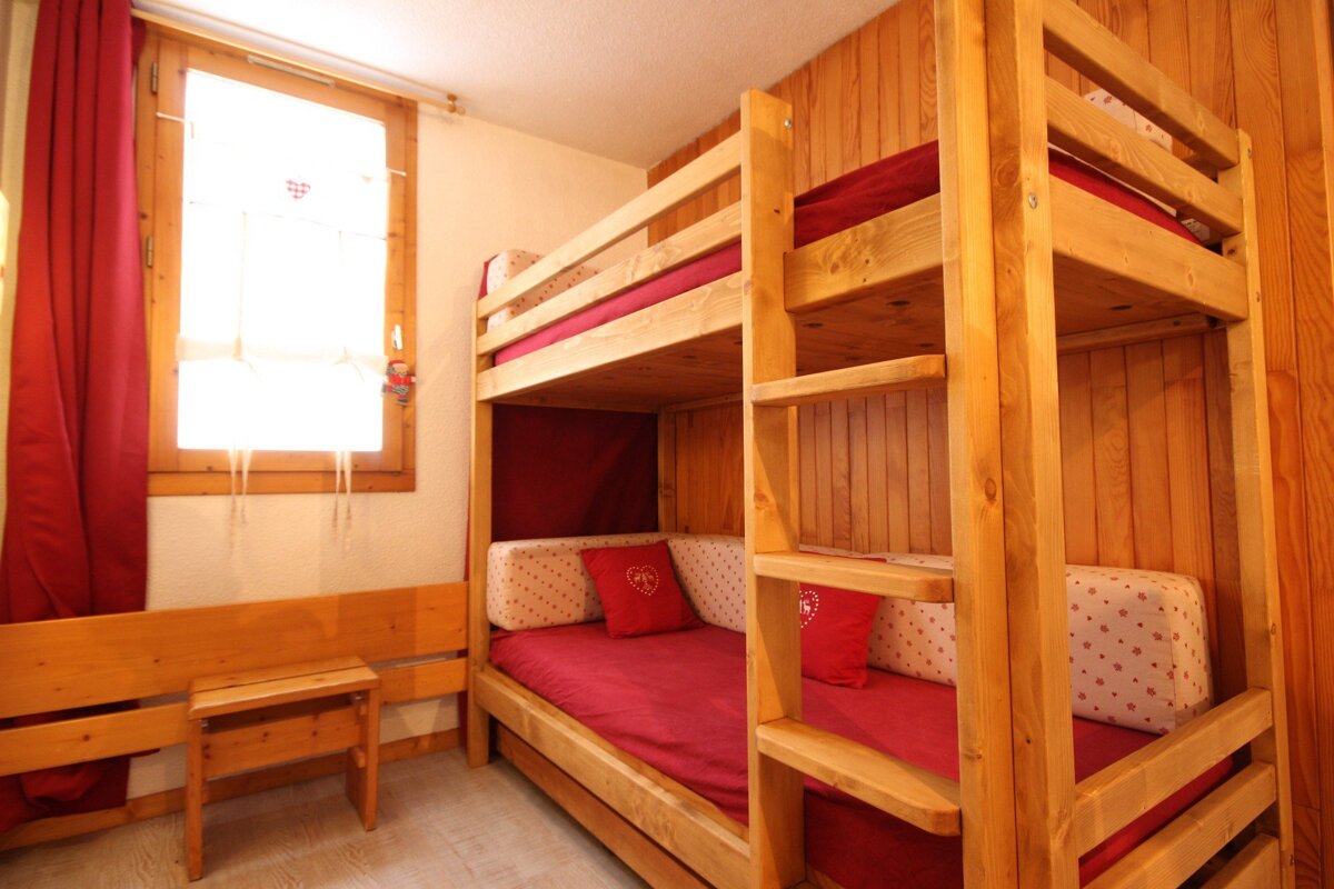 A wooden bunk bed with red sheets and white pillows