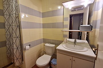 A tiled bathroom featuring yellow and gray horizontal stripes. It includes a toilet, sink with vanity, and a shower with a patterned curtain.