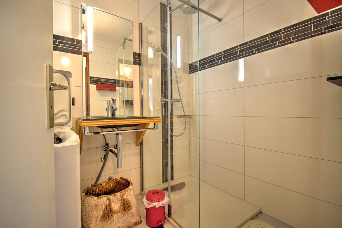 Modern bathroom featuring a walk-in glass shower, a floating sink with a wooden counter, a woven basket, and a red trash can.