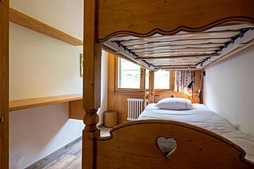 A small, rustic bedroom featuring a wooden bunk bed with a heart cutout on the footboard, next to a window.