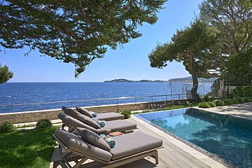 A swimming pool surrounded by lounge chairs overlooking the ocean