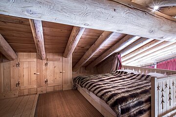 A cozy, all-wood rustic bedroom with exposed beams, a sloped ceiling, and a bed with a warm, striped fur blanket.