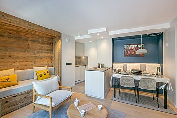 Modern open-plan apartment with a cozy living area featuring a wooden wall, a functional kitchen island, and a dining space with a blue accent wall.