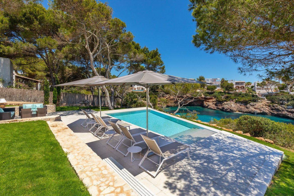 A swimming pool surrounded by chairs and umbrellas with a view of the ocean