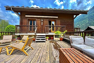 A wooden deck with chairs and a couch in front of a house