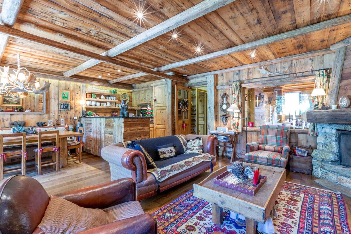 Cozy, rustic cabin interior featuring wood-paneled walls and ceilings, comfy seating, a colorful rug, and alpine-style decor.