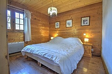 Rustic cabin bedroom with wood-paneled walls and ceiling, featuring a large bed with a white duvet and warm bedside lamps.