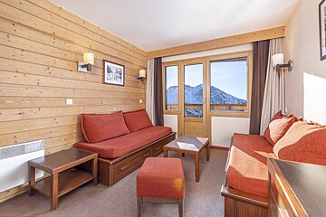 Cozy, wood-paneled room with red sofas and a coffee table, featuring a large window with a stunning view of snow-capped mountains.