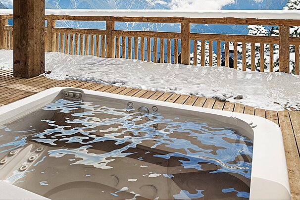 A hot tub on a snowy deck with mountains in the background