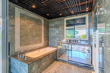 Elegant bathroom featuring green marble, a built-in tub, mirrored vanity, and a striking black grid ceiling, reflecting outdoor views.