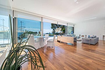 Spacious, modern living room with floor-to-ceiling windows offering a stunning sea view. Features a dining area, lounge, and warm wooden floors.