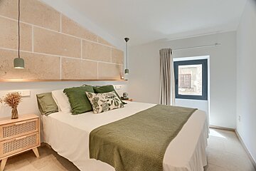 A bright, modern rustic bedroom featuring a white bed with green accents, a unique stone accent wall, and a window with natural light.