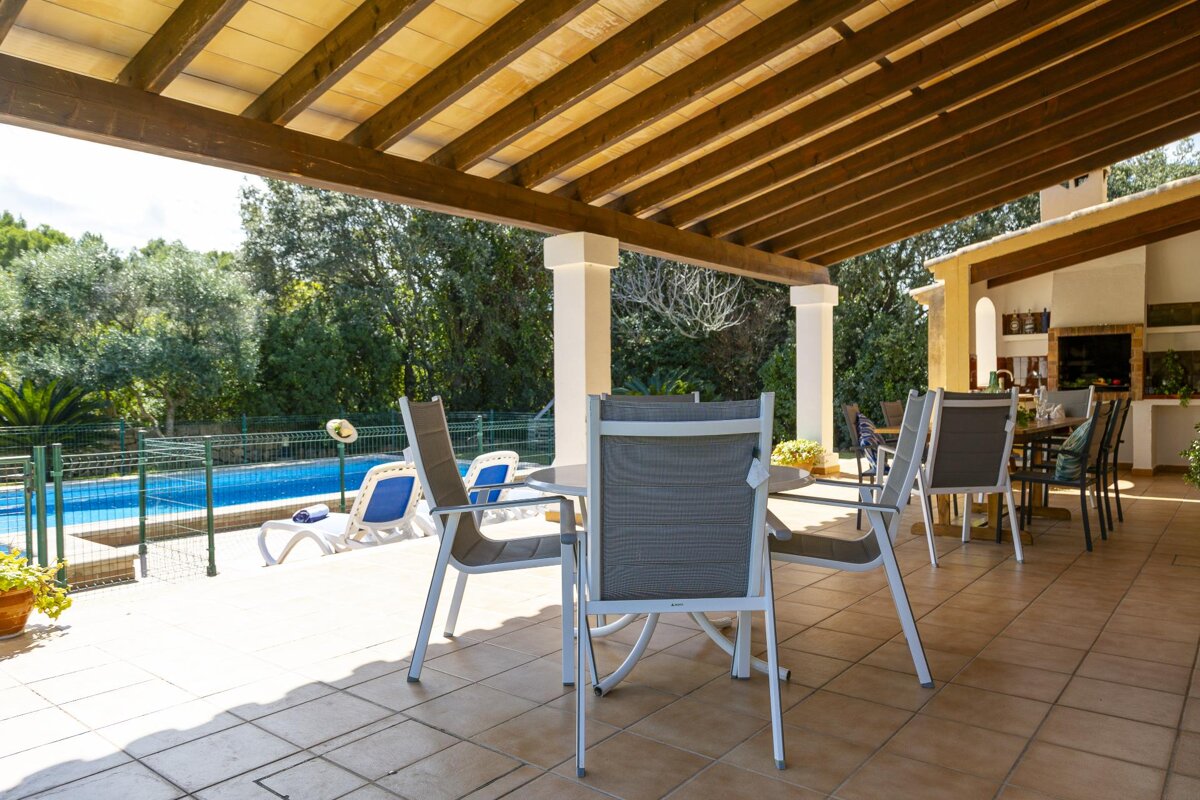 A table and chairs on a patio with a pool in the background