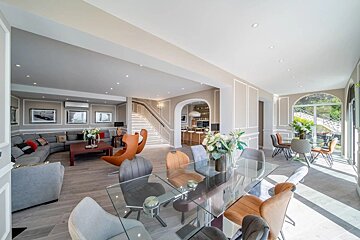 Spacious modern open-plan home featuring a glass dining table with colorful chairs and a cozy grey living room area.