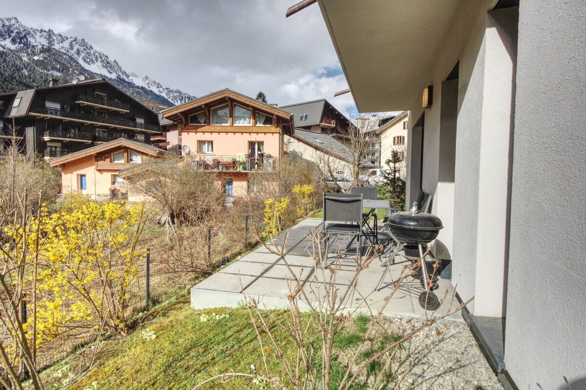A patio with a grill and chairs in front of a house with mountains in the background