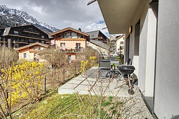 A patio with a grill and chairs in front of a house with mountains in the background