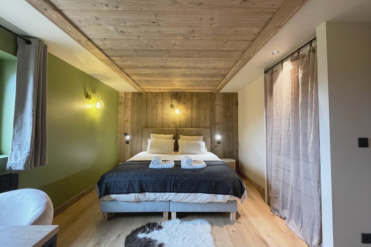 A cozy, rustic bedroom with a wooden ceiling and accent wall, a green side wall, a double bed, and light wood floors.