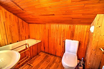 A cozy, wood-paneled bathroom with a bathtub, toilet, and sink, featuring warm orange-brown wooden walls, floor, and a sloped ceiling.