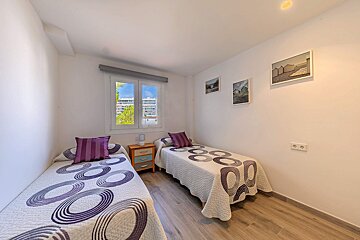 Two beds in a bedroom with purple pillows on them