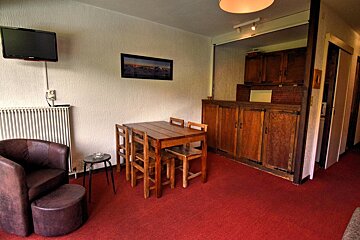 Cozy room featuring red carpet, a leather armchair, wooden dining set, wall-mounted TV, and a rustic wooden cabinet.