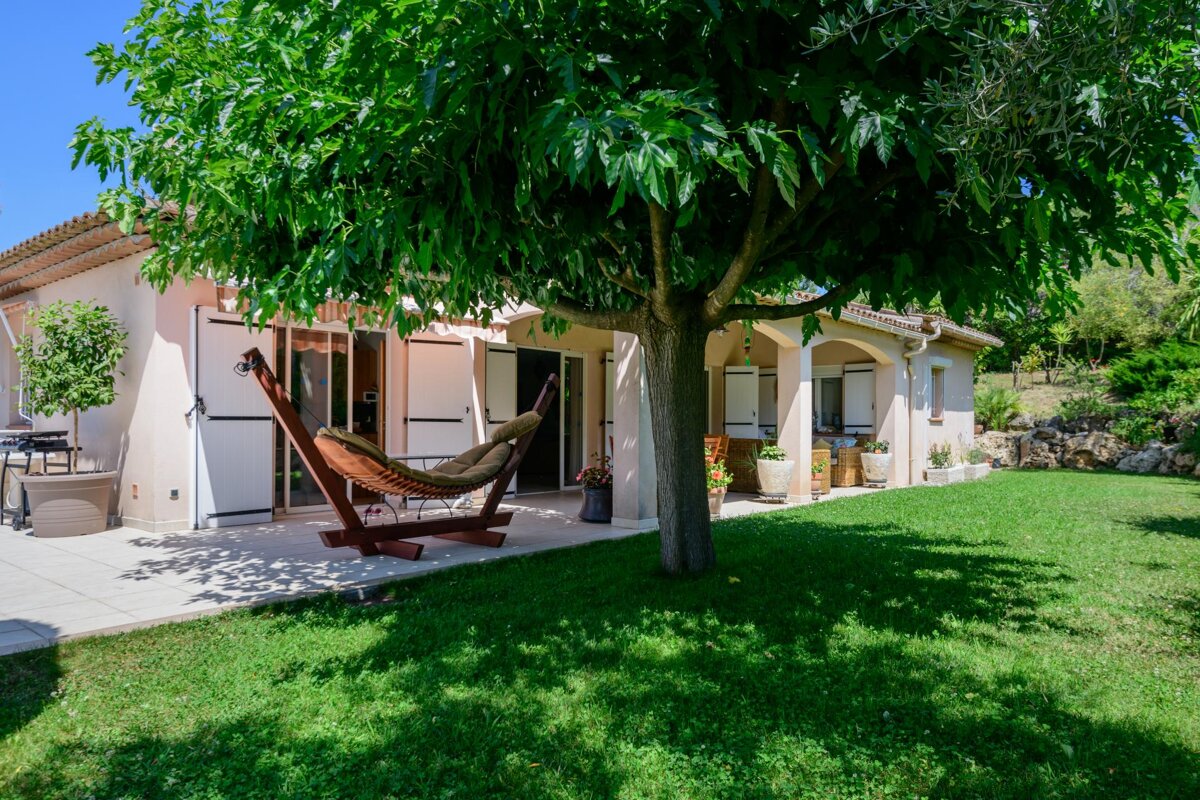 A hammock sits under a tree in front of a house
