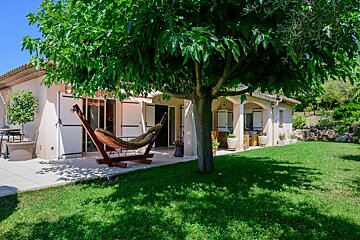 A hammock sits under a tree in front of a house