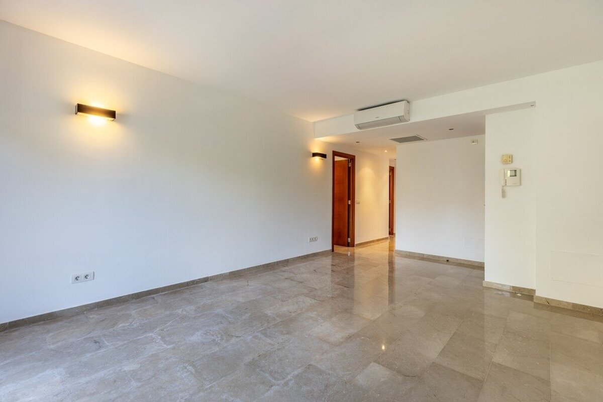 An empty room with polished marble floors, white walls with glowing wall lamps, and a doorway leading to a hallway.